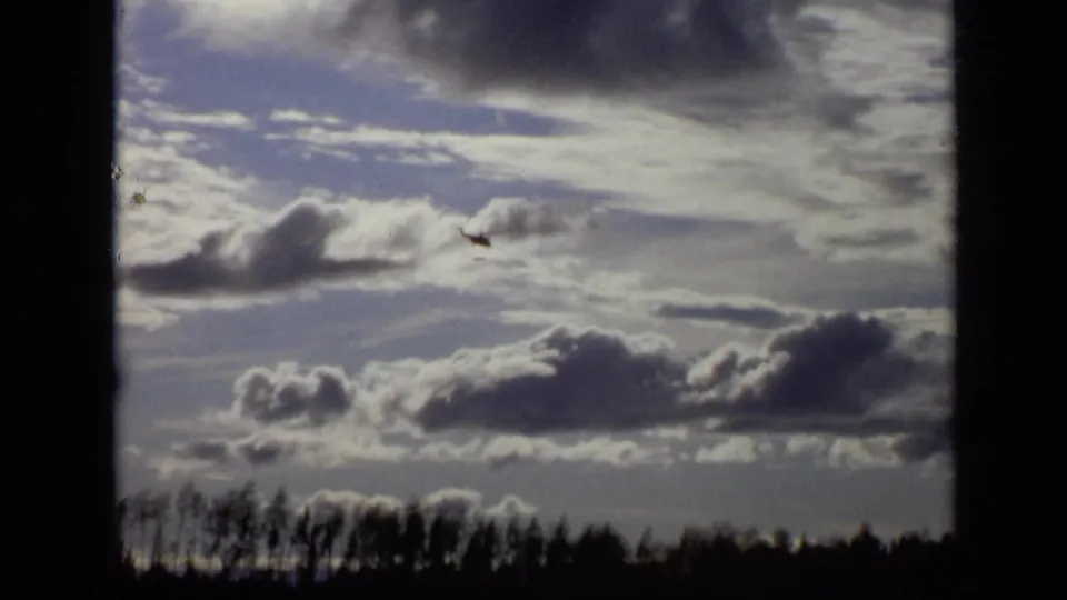 A small helicopter appears against dramatic clouds above a treeline in 1971 Moscow 8mm footage.
