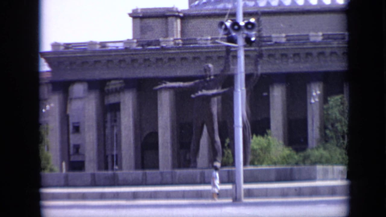 Columned building facade, streetlight, sidewalk, pedestrians, and foreground roadway.