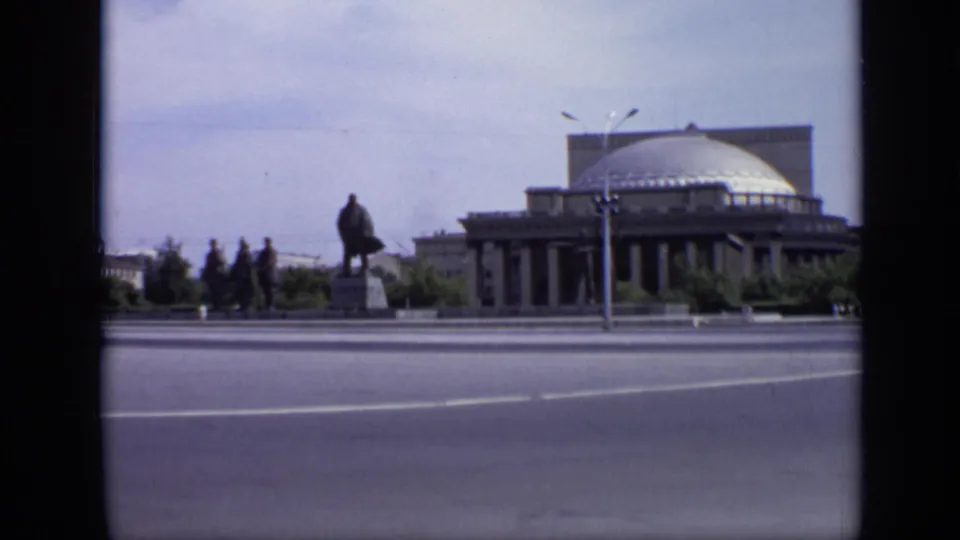 1971 Moscow 8mm frame showing a wide road, domed public building, statue on a pedestal, trees, and small distant figures.