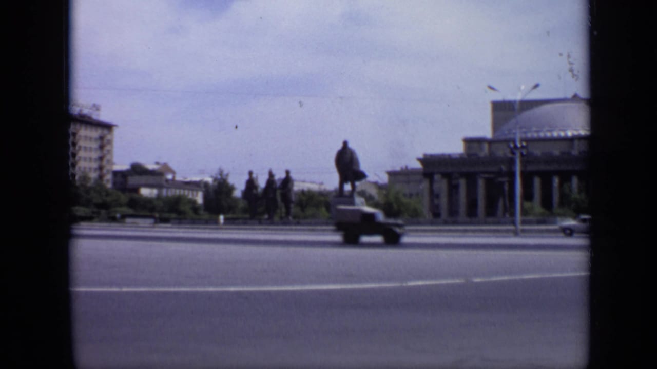 Street view with statue, domed building, apartment block, road, and passing car.