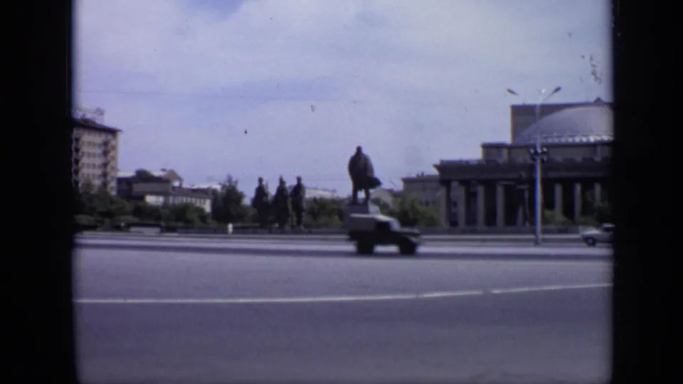 1971 Moscow frame with a statue in the square, domed building at right, apartment block at left, and a car moving through the road.