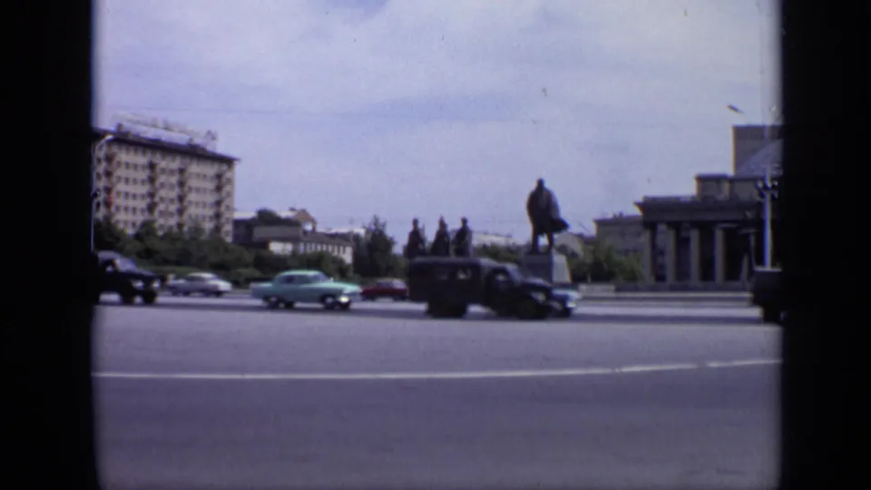 1971 Moscow 8mm frame with several Soviet-era cars on a broad road, a statue in the square, an apartment block, trees, and building edge at right.