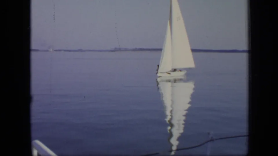 1971 Moscow 8mm frame showing a small white sailboat reflected on calm water, with a low distant shoreline under a pale sky.