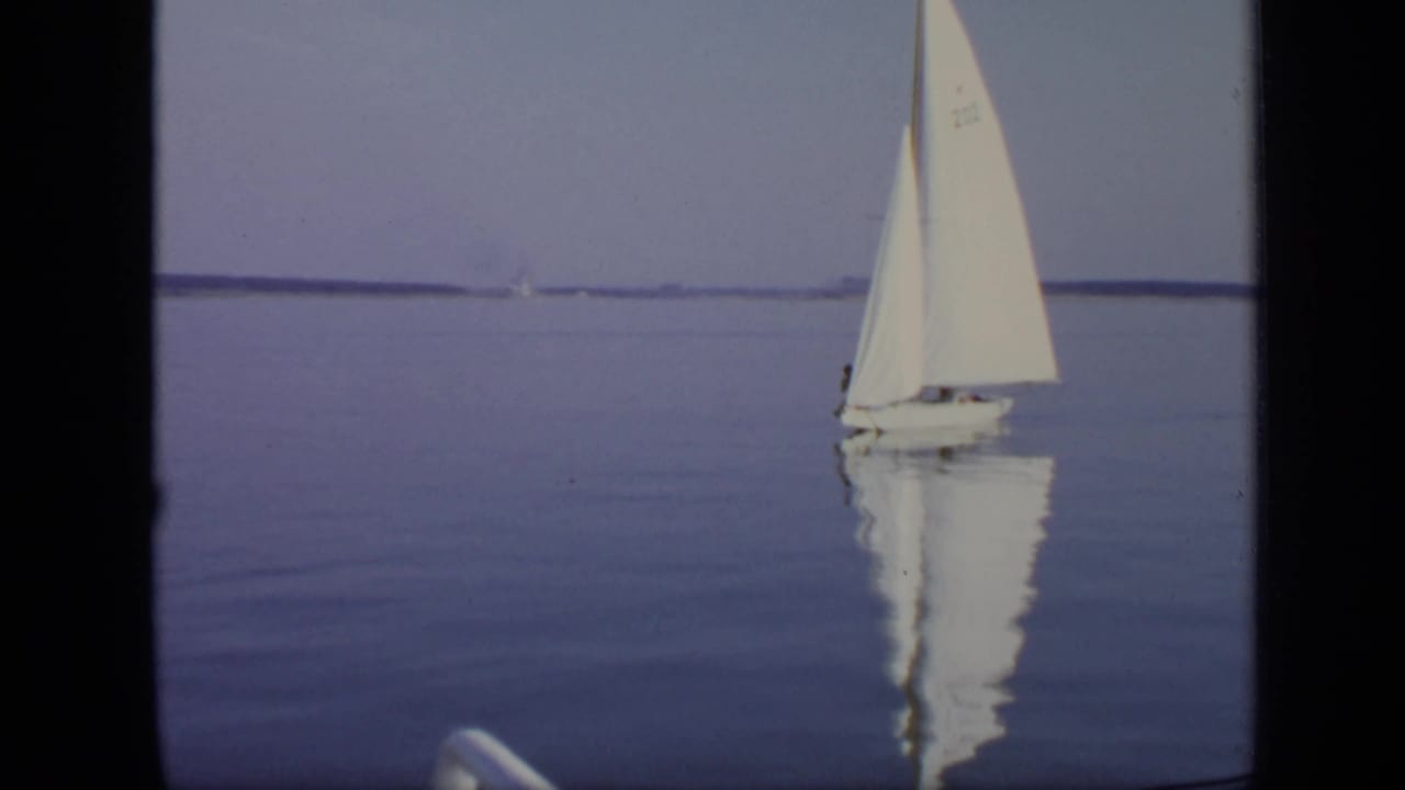1971 Moscow 8mm frame showing a small white sailboat gliding across calm lake water with a soft reflection.