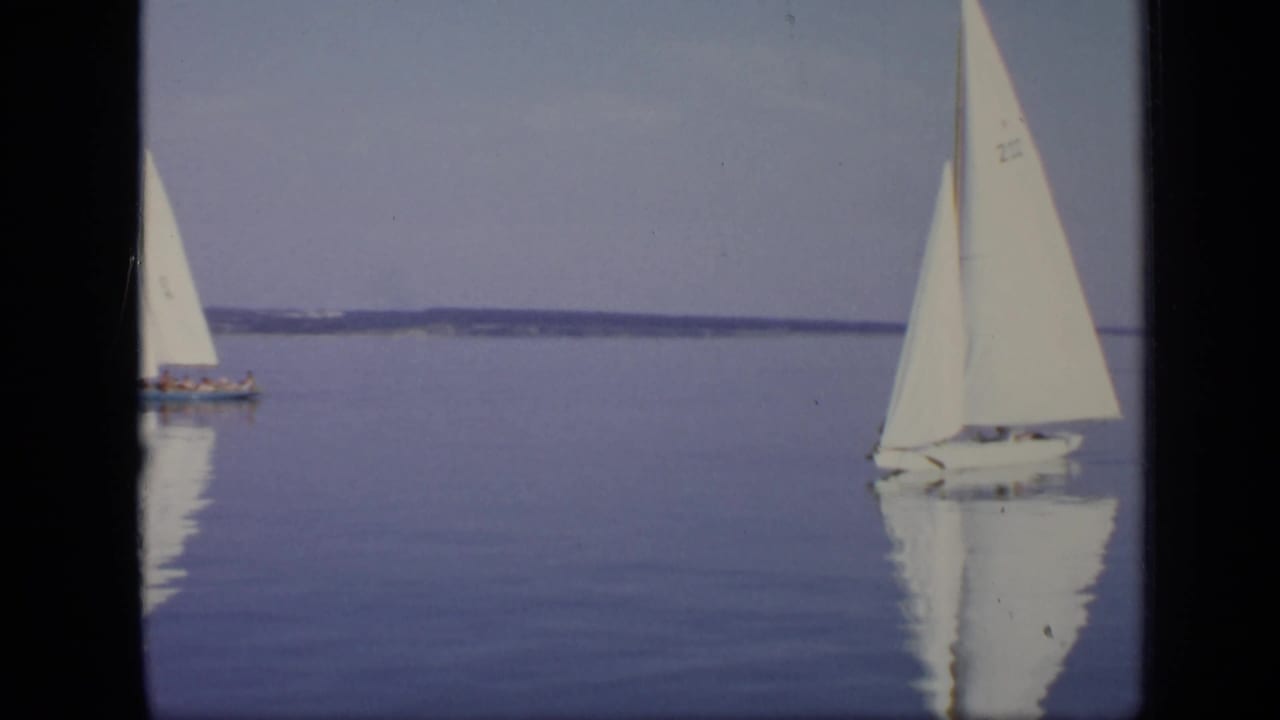 Two small sailboats on calm water, one nearer the right edge with a white sail.