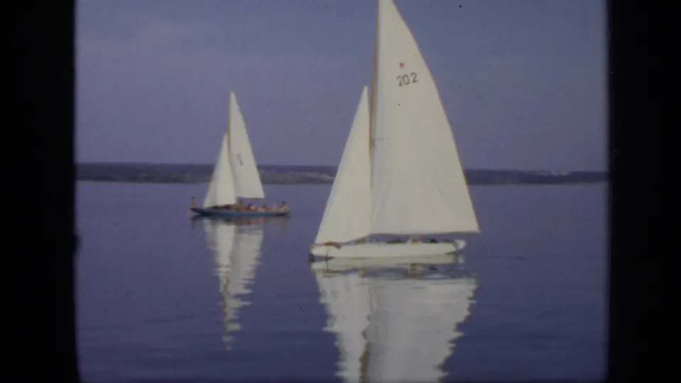 1971 Moscow home-movie frame of two small sailboats on a calm lake, including a nearer sail marked 202 and a red star.