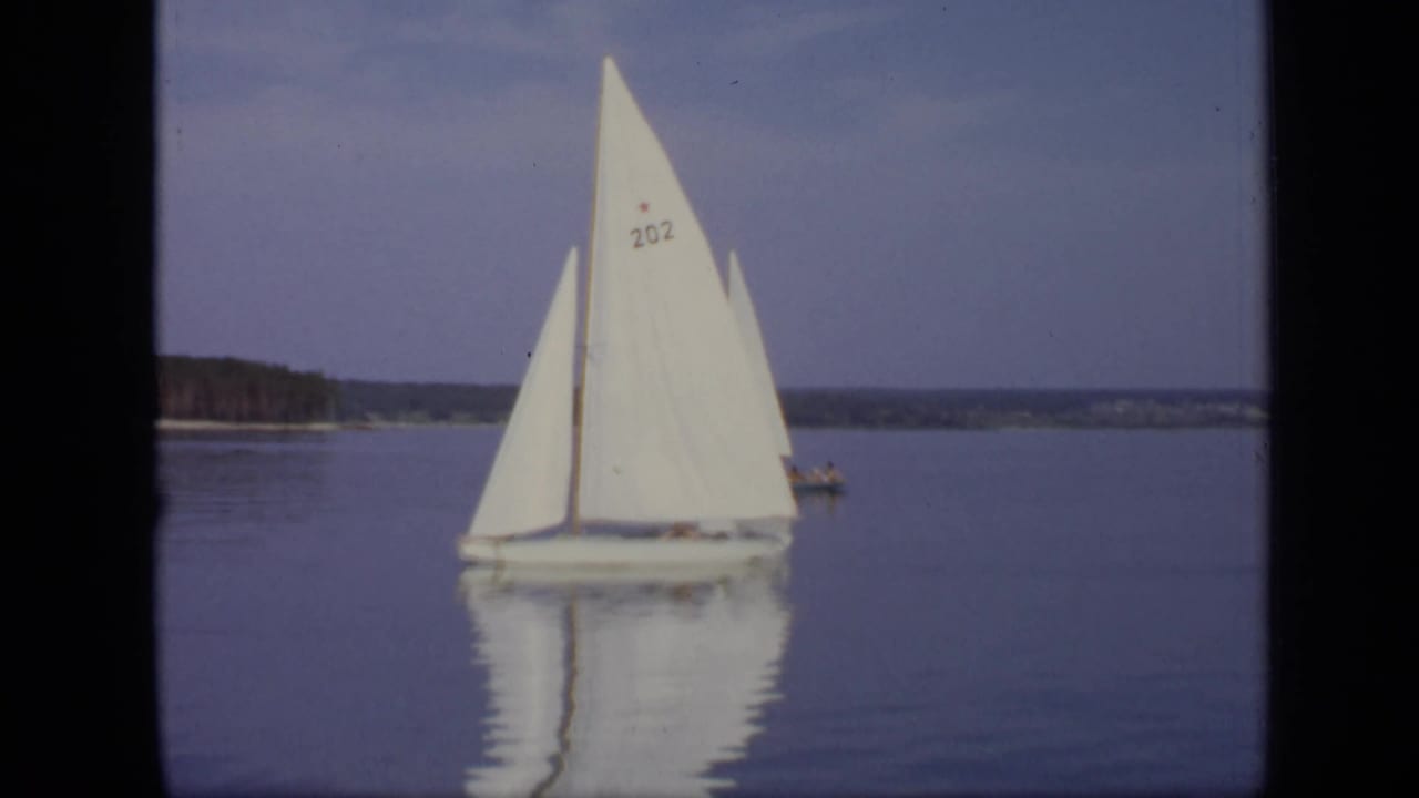 A white sailboat marked 202 passes on calm water in supported 1971 Moscow lake footage.
