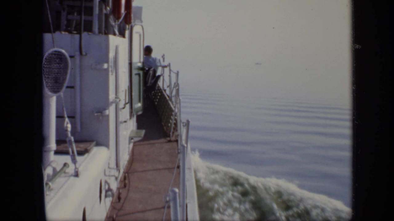 White ship side and railing with water wake spreading behind it.