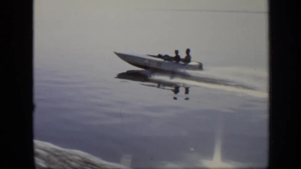 A white speedboat with two visible occupants speeds across calm water in the 1971 Moscow river footage.