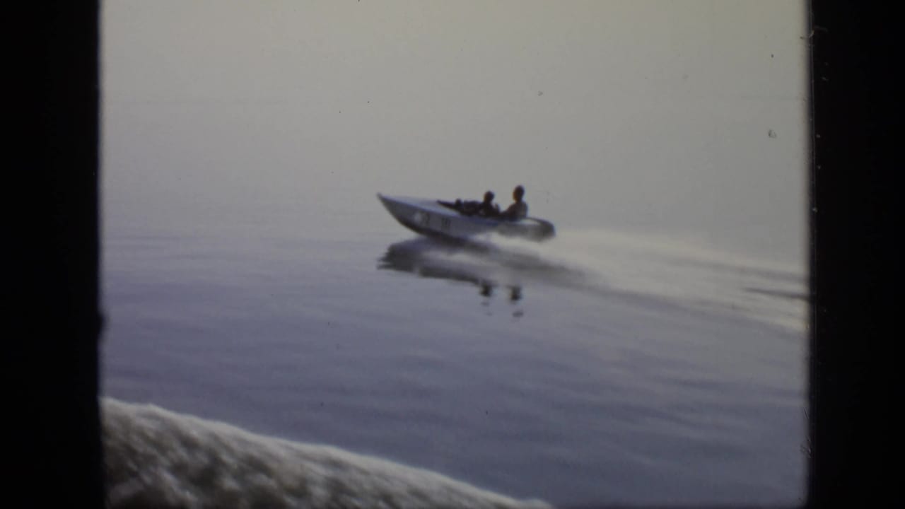 Small motorboat with two riders speeding across calm water.