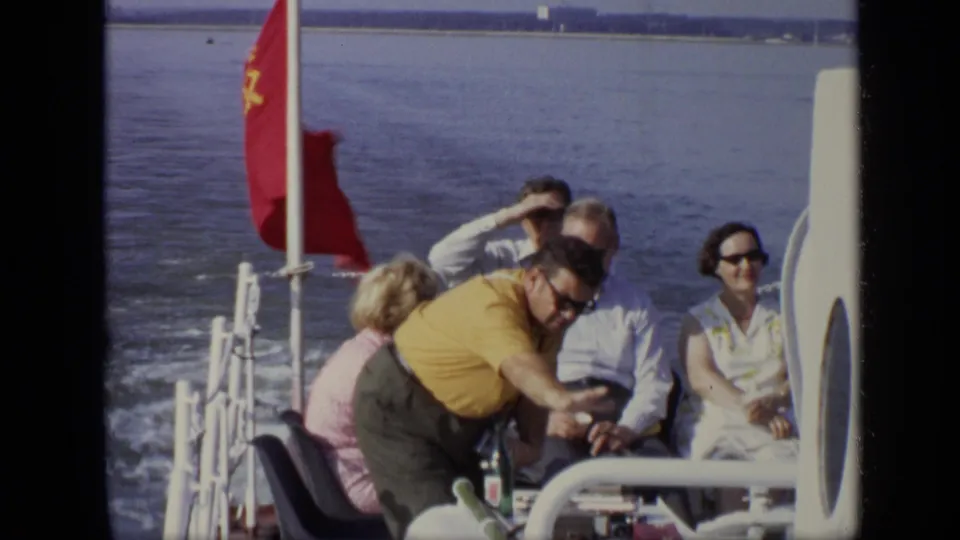 Closer 1971 Moscow deck view of adults seated by a red flag as a man in a yellow shirt turns toward the camera.
