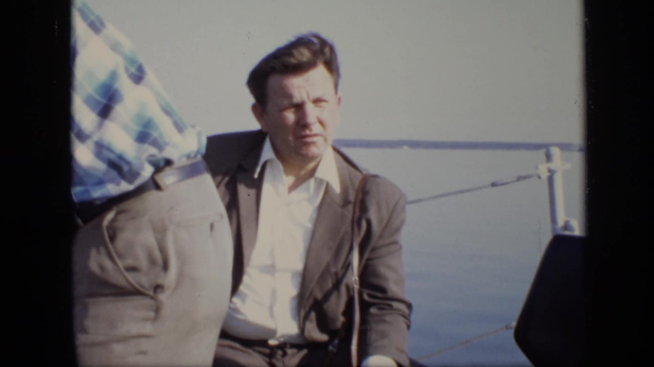1971 Moscow riverboat frame with a seated man in a brown suit on deck, partly obscured by another passenger.