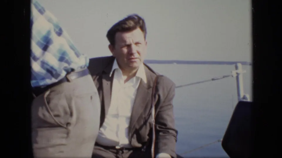 1971 Moscow riverboat frame with a seated man in a brown suit on deck, partly obscured by another passenger.