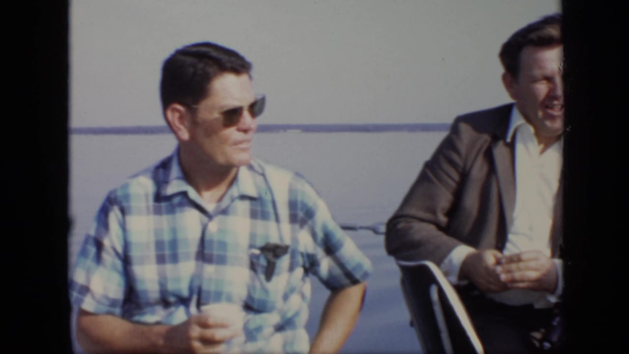 Two men seated on a boat with open water behind them.