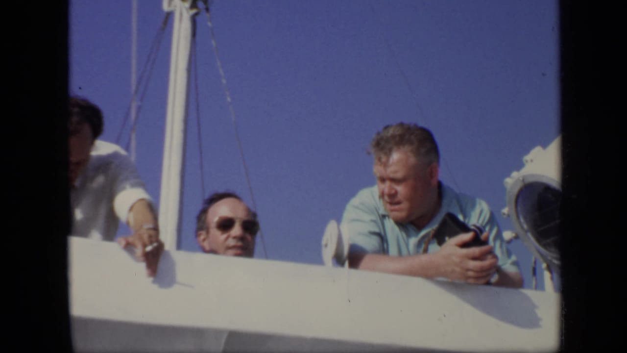 1971 8mm Moscow boat scene with three adult men behind the rail, including a man with sunglasses and a man holding a camera.