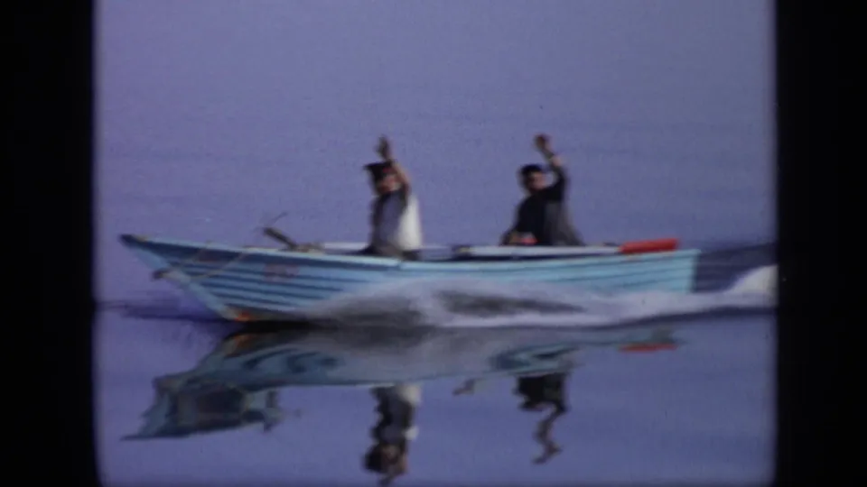 1971 Moscow 8mm frame showing a blue motorboat in motion as one of the two men raises an arm toward the camera.