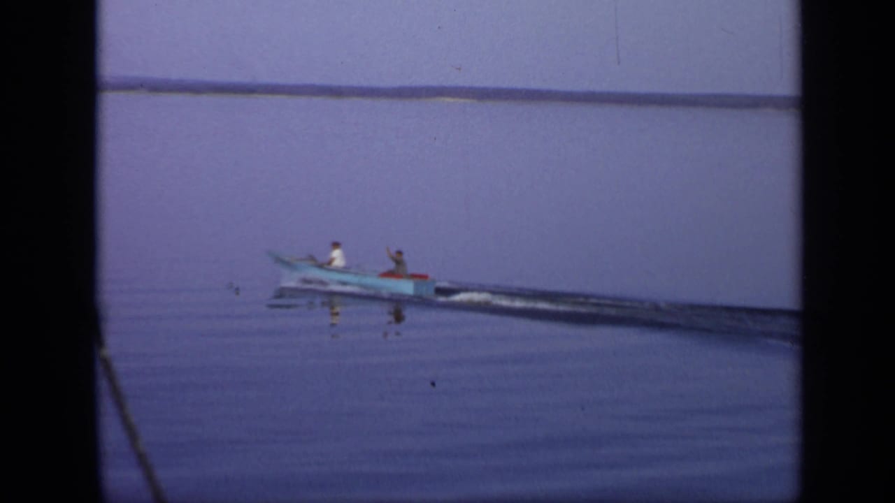 A small motorboat carries two people away across open water.