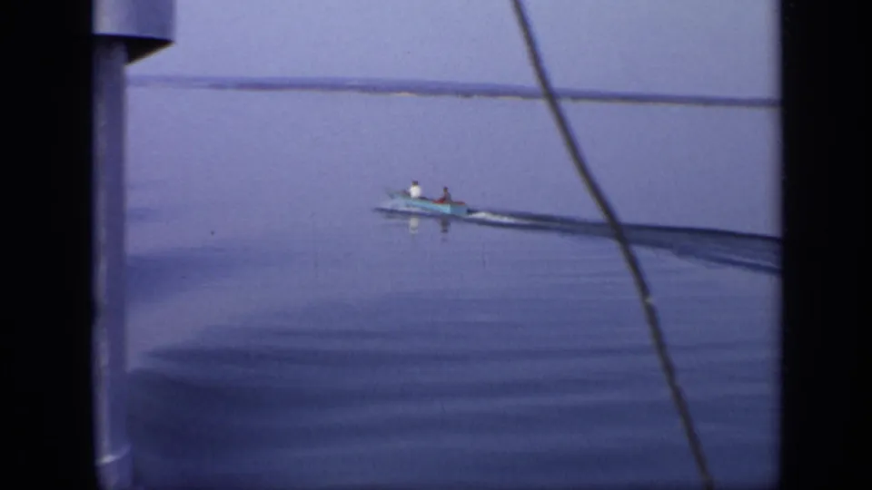 A distant small boat crosses calm water, partly framed by dark film edges or nearby structure in the 1971 Moscow clip.