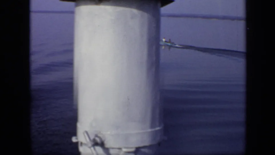 A white cylindrical post dominates the foreground while the small boat continues away on calm water in the supported Moscow footage.