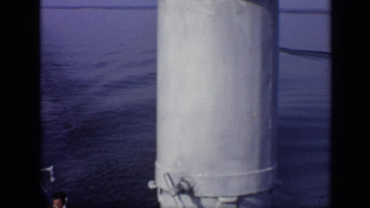 Boat deck seen through dark film edges, with white cylindrical structures and water behind.