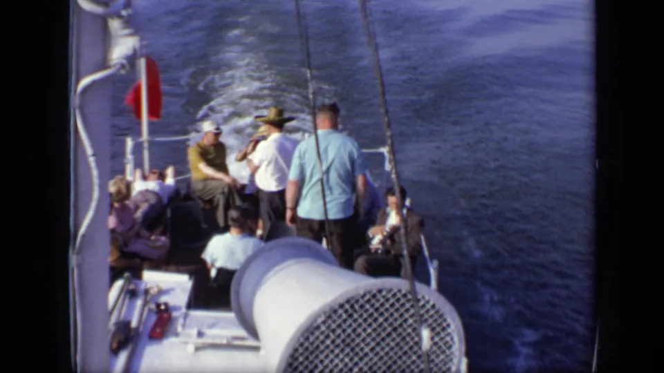 1971 8mm frame from Moscow, Russia showing passengers on a boat deck, a red flag, white railings, rigging, and water behind.