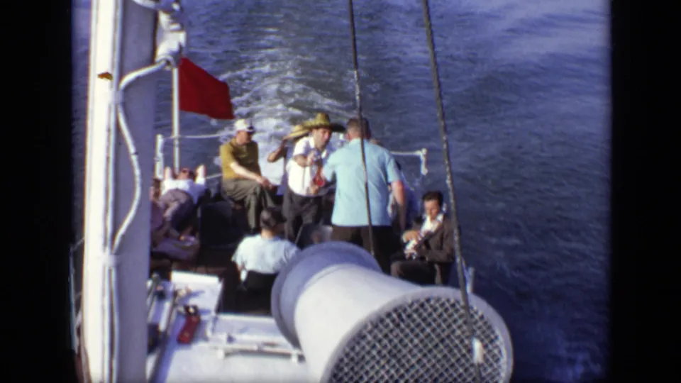 1971 8mm home-movie frame showing a group aboard a boat in Moscow, Russia, with a red flag and wake in the background.