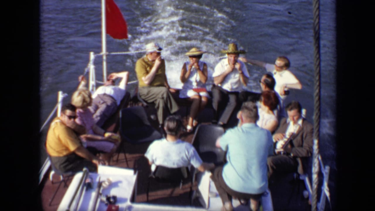 Passengers sit on the rear deck of a moving boat with water wake behind them.