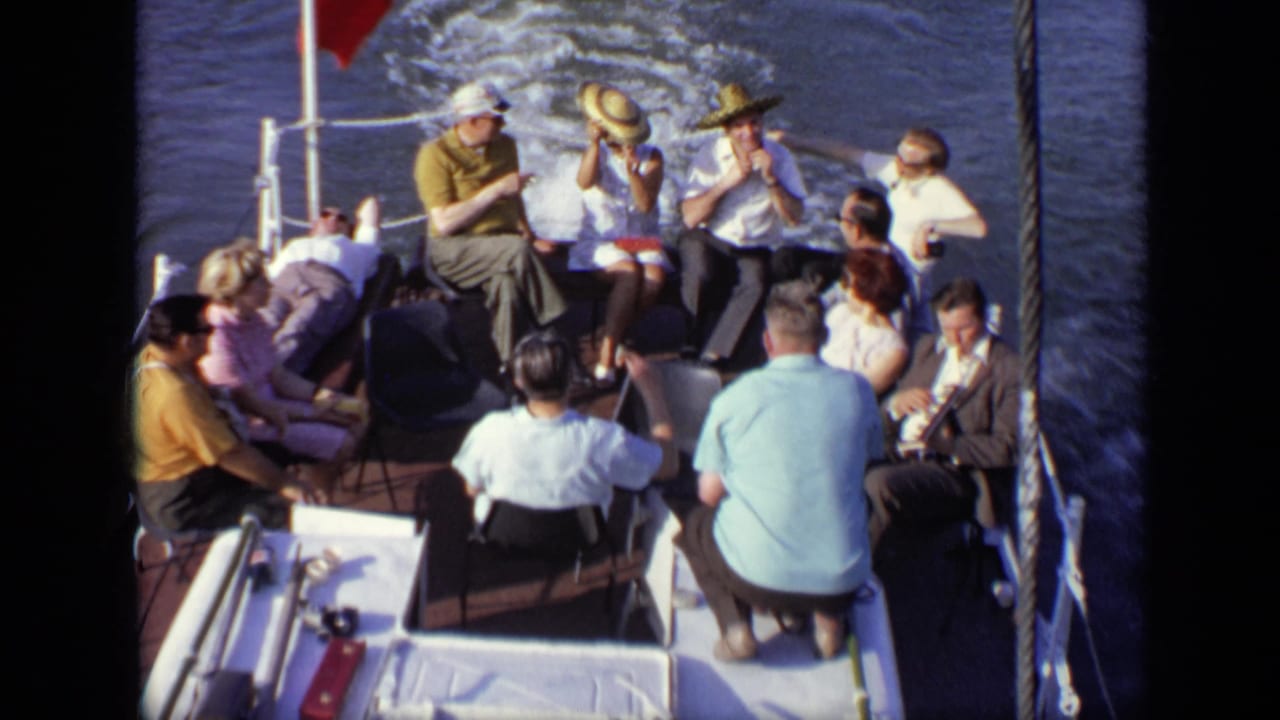 Group of adults sits and stands on a boat deck while the wake trails behind.