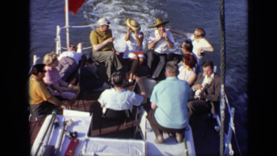 Adults in summer clothing gather on the rear deck of a moving boat in Moscow, with chairs, railings, and dark water visible.