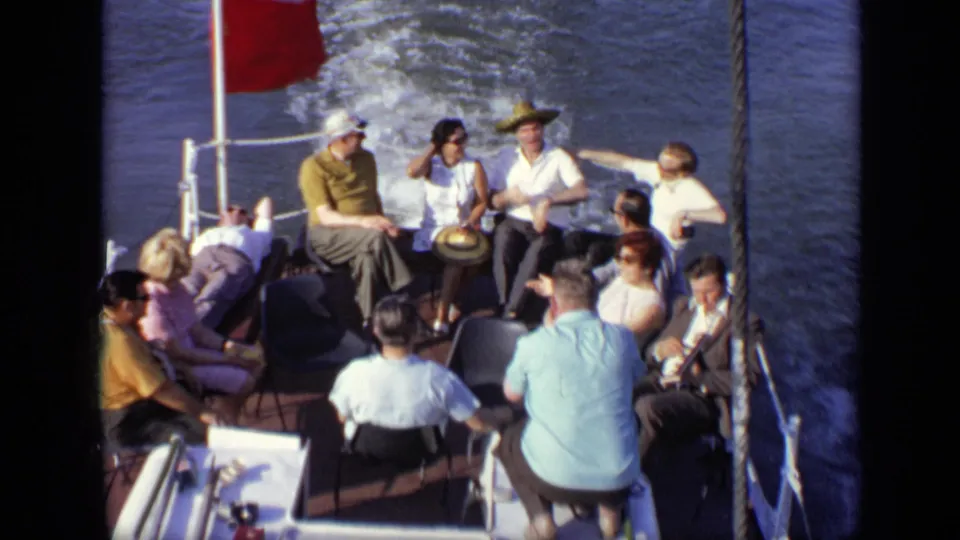 Final 1971 Moscow boat frame showing a relaxed group on the stern deck, with a red flag, railings, and water wake in view.