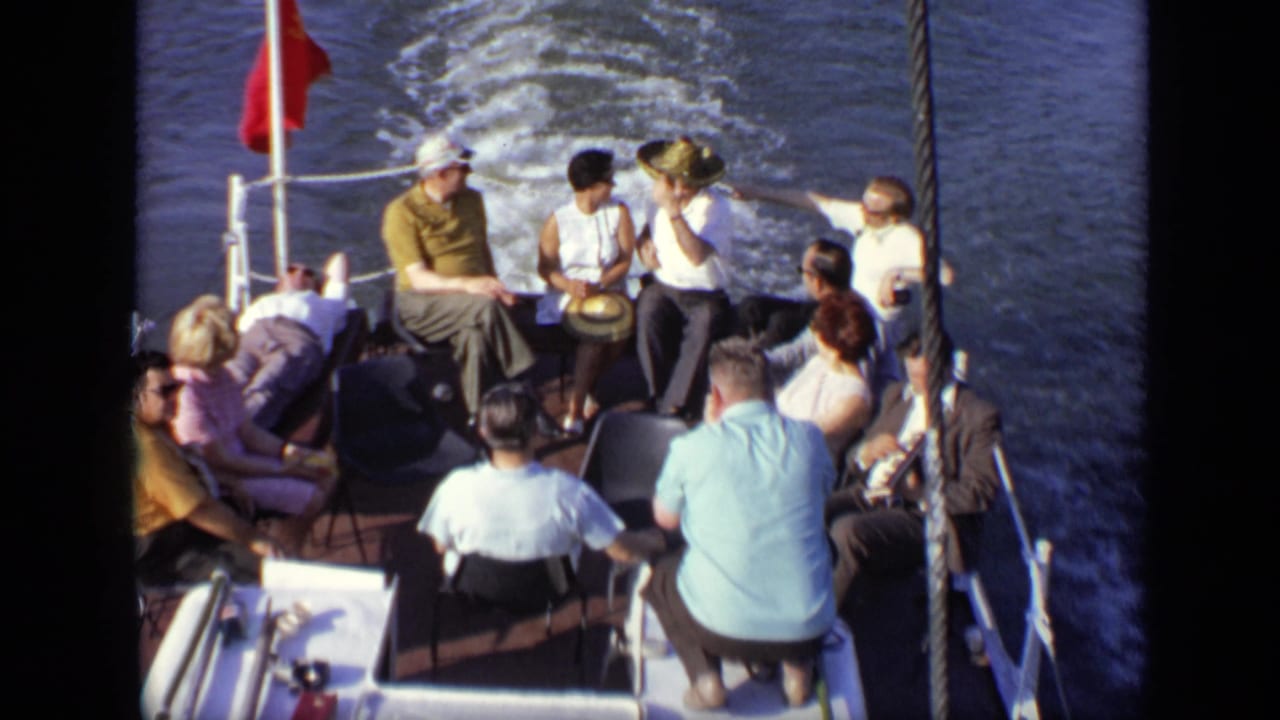 Adults seated on a small boat deck with a red flag and water wake behind them.