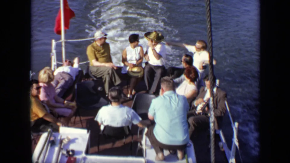 1971 Moscow home-movie frame showing adults relaxing on a small boat deck as the vessel leaves a wake behind.