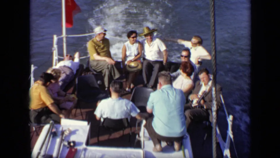 Sunlit 1971 Moscow boat scene with adults seated on deck chairs while the wake trails behind the boat.