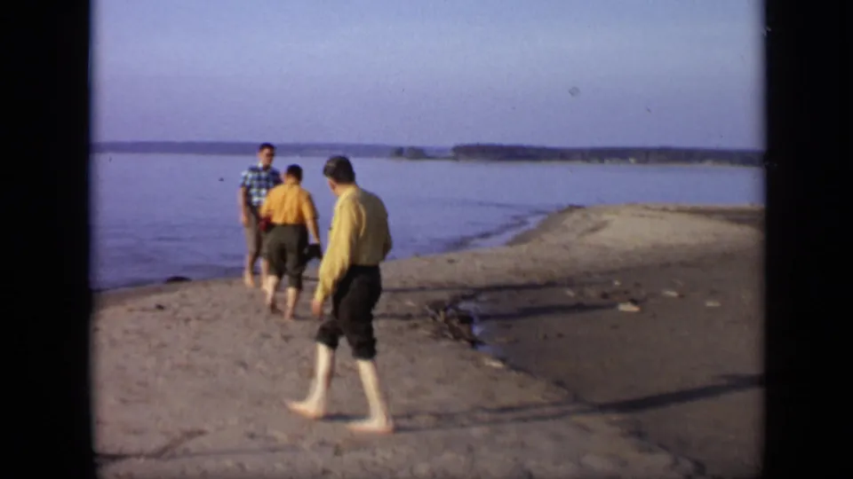 1971 Moscow-area riverbank frame with men gathered near the water as a barefoot man passes in the foreground.