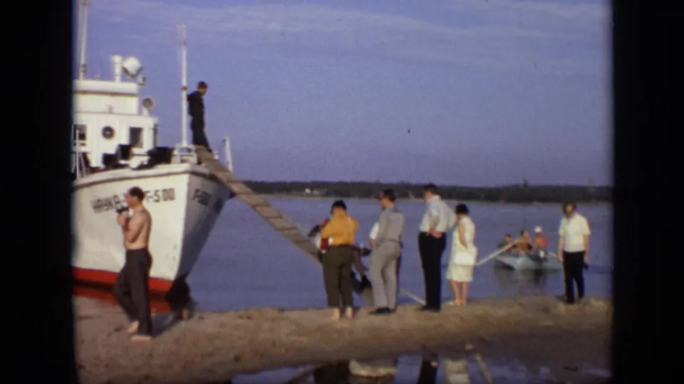 1971 Moscow riverbank scene with a docked white boat, people waiting near the ramp, and passengers visible near a small boat on the water.