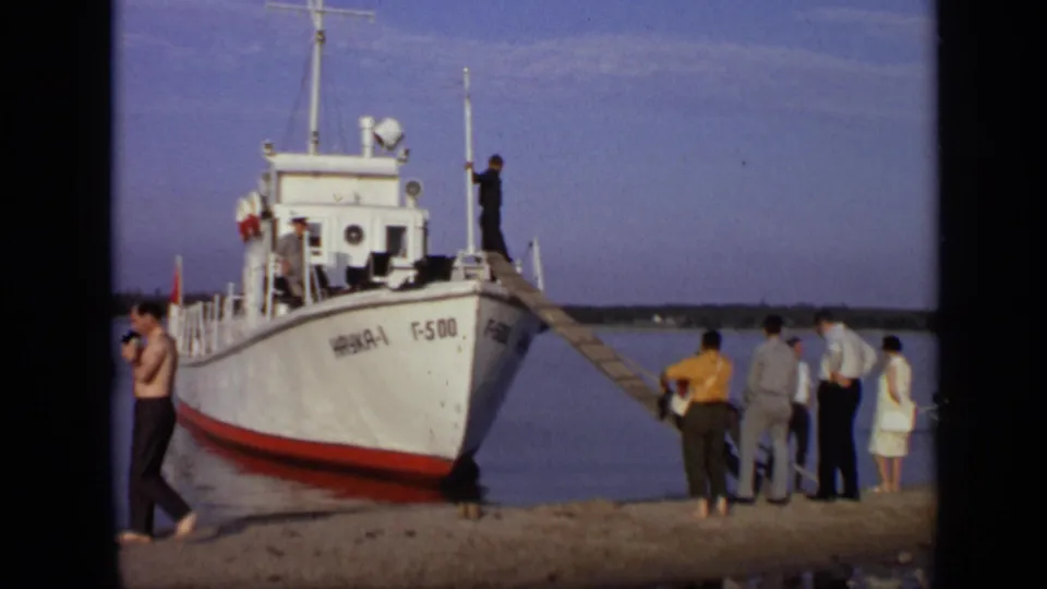 1971 Moscow footage frame showing the bow of a white boat marked F-500, a wooden gangway, and several adults gathered by the water.
