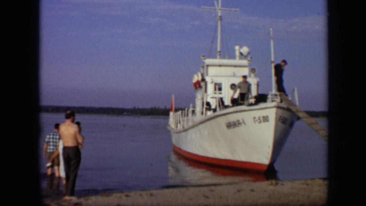 People stand on a sandy shore beside a white boat at calm water.