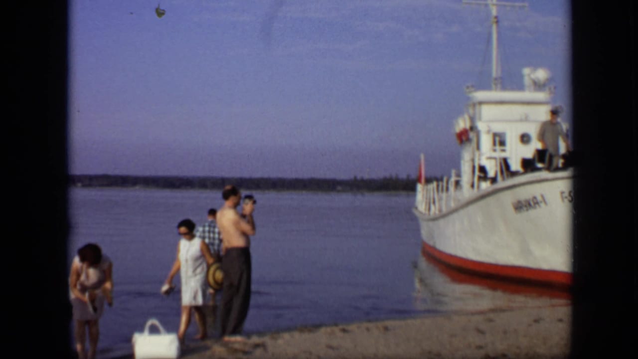 A small group stands near the water as the bow of a white boat fills the right side.