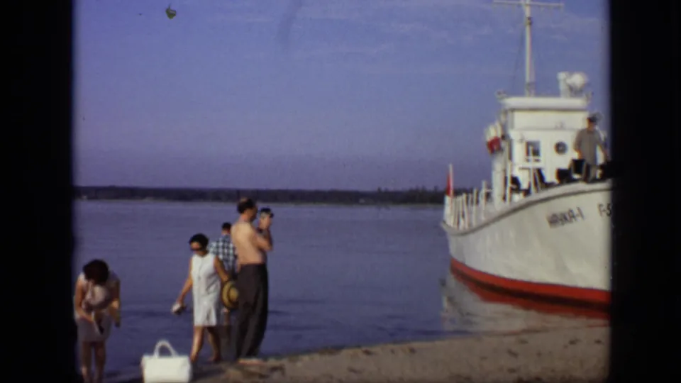 1971 Moscow waterfront frame with adults in summer clothing near the bow of a white marked boat.