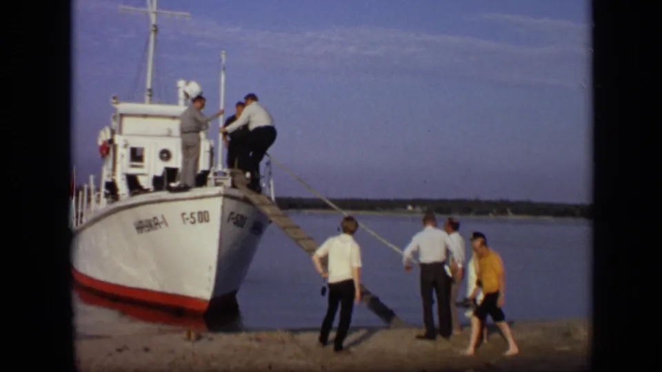 1971 Moscow home-movie frame with passengers boarding a marked white and red vessel from a simple wooden gangplank.