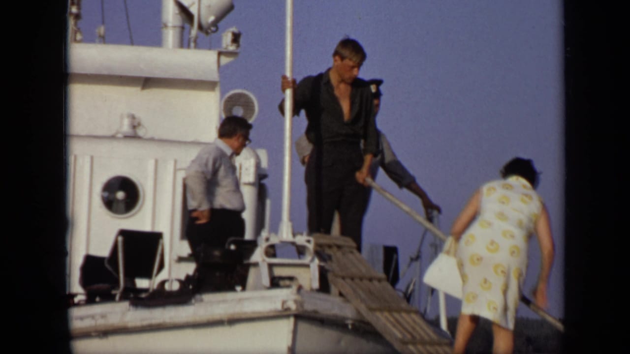 Adults boarding a white boat from a wooden plank beside calm water.