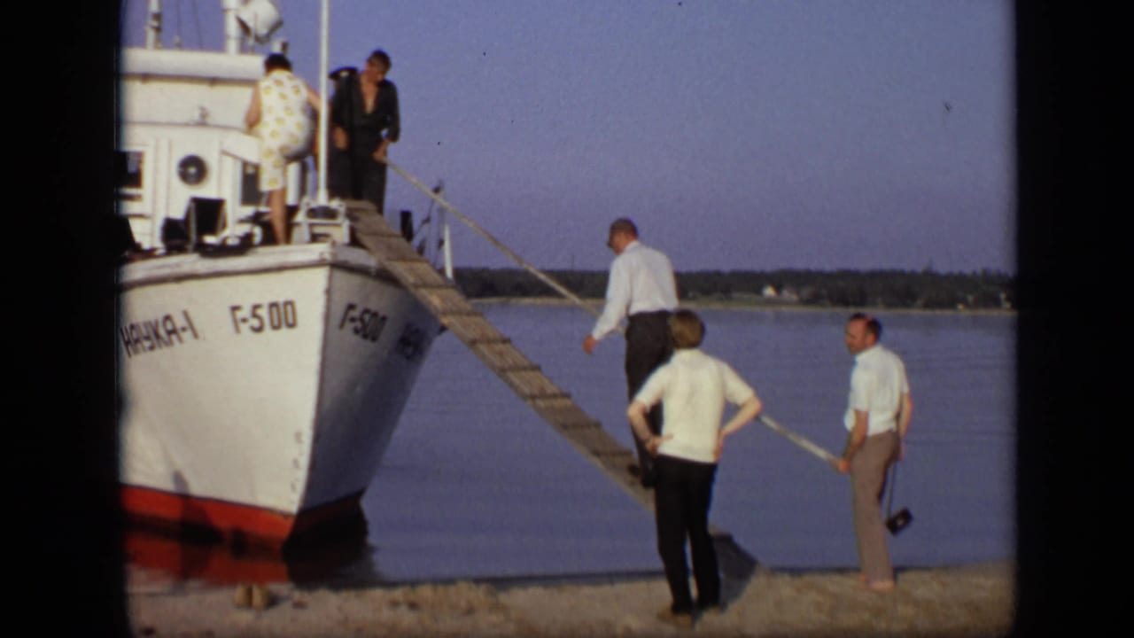 Small white boat at the riverbank with adults boarding by plank.