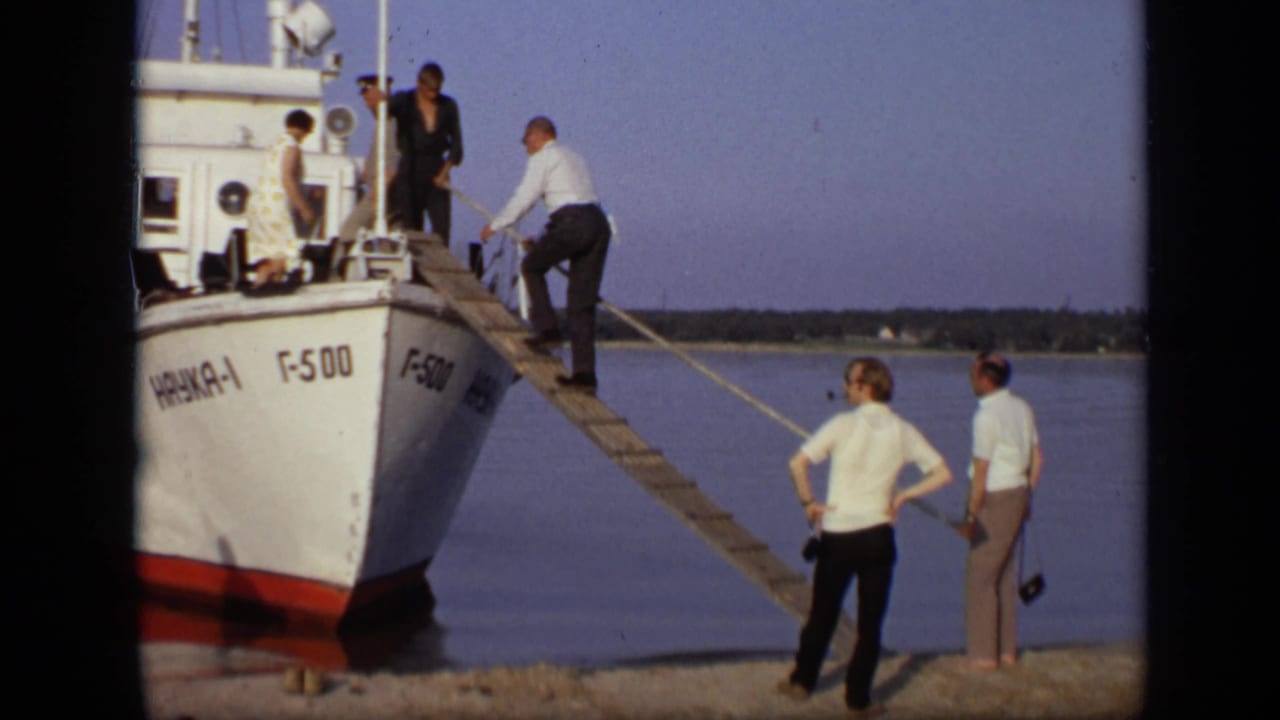 Adults gather as a man steps onto a wooden gangplank leading to a white boat.