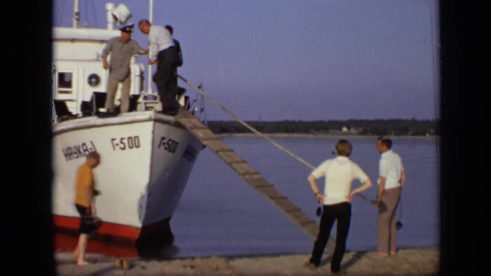 1971 8mm frame of a man stepping from a wooden gangplank onto a white boat with Cyrillic markings near Moscow.
