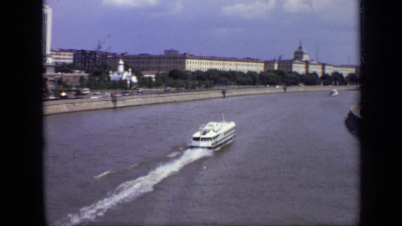 1971 Moscow 8mm frame showing a white ferry speeding along a broad river below large tree-lined buildings.