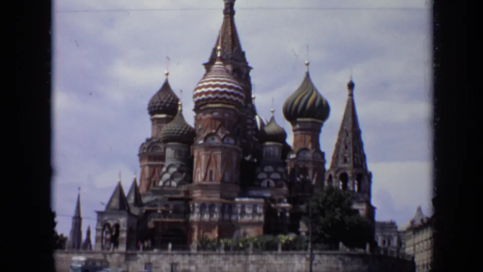 1971 Moscow home-movie frame showing St. Basil's Cathedral from a slightly lower visitor angle, with domes, spires, and surrounding trees.