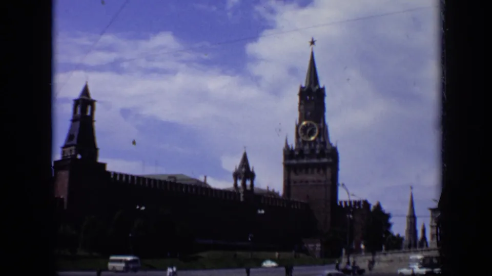 1971 Moscow home-movie frame showing the Kremlin wall and Spasskaya Tower from street level, with vehicles and pedestrians below.