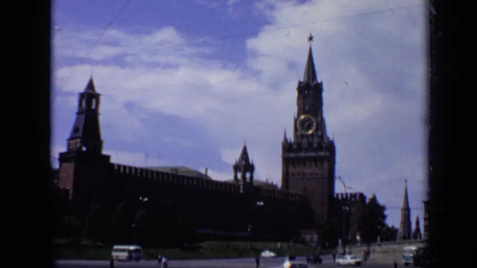 1971 Moscow frame with Spasskaya Tower, the Kremlin wall, street traffic, and distant pedestrians under bright clouds.