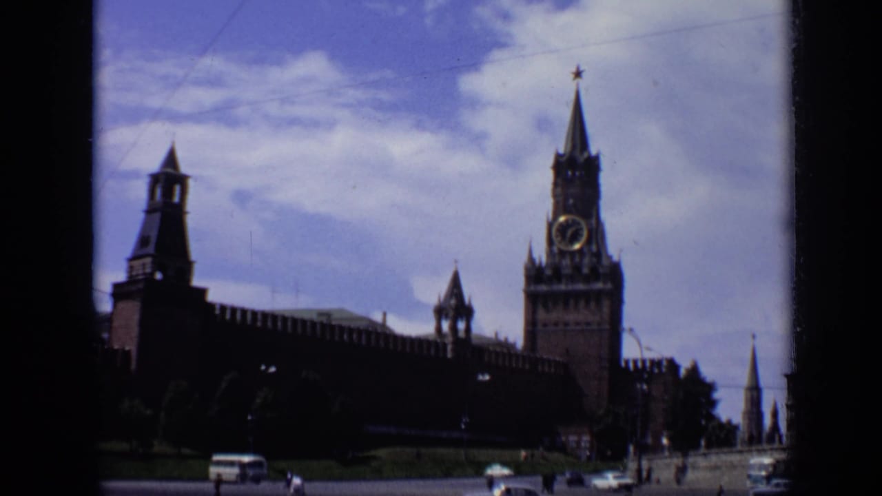 1971 Moscow 8mm frame showing the Kremlin wall, Spasskaya Tower, cloudy sky, and small vehicles near the foreground.