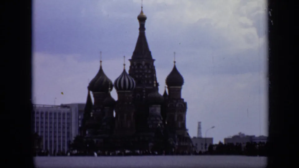 1971 Moscow 8mm frame showing St. Basil's Cathedral, onion domes, an adjacent urban building, and small figures across the square.
